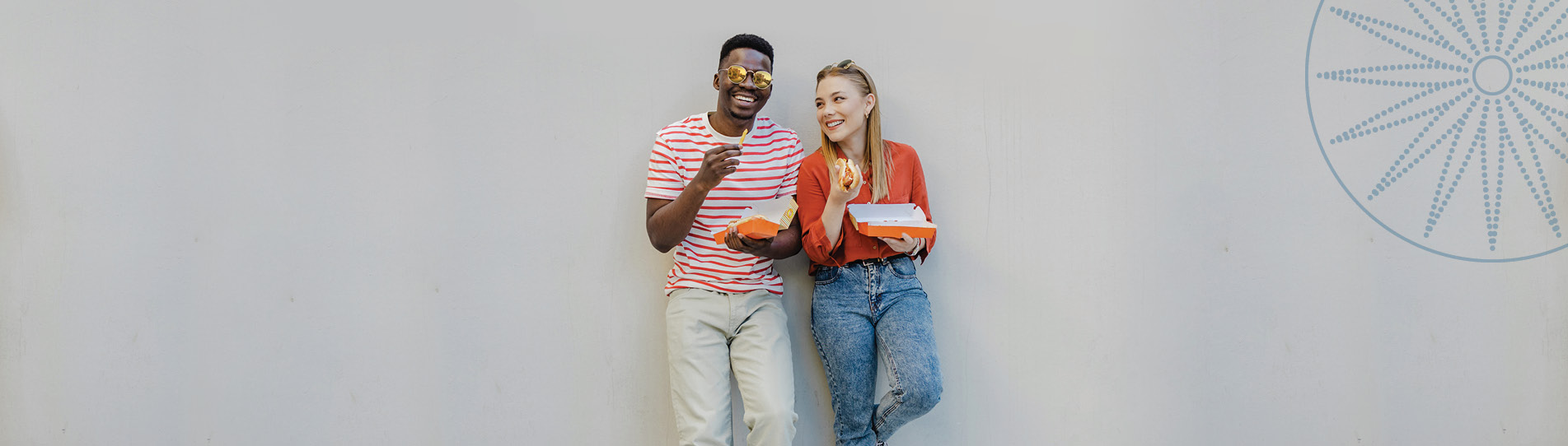 two friends laughing and having lunch leaning on the wall of a building